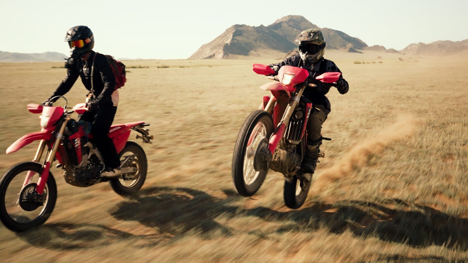 Two riders pushing Honda CRF450RL dual-sport motorcycles across the open steppe